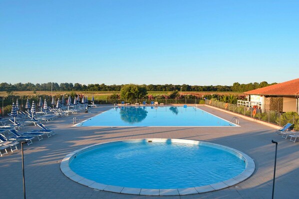 A large rectangular swimming pool with a smaller circular section, surrounded by lounge chairs and umbrellas, with a clear view of the surrounding landscape.