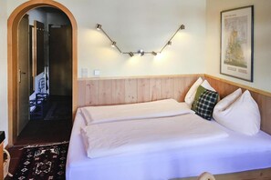 Quarto de hotel com cabeceira de madeira, cama com roupa de cama branca, luminária fixada na parede e quadro emoldurado.
