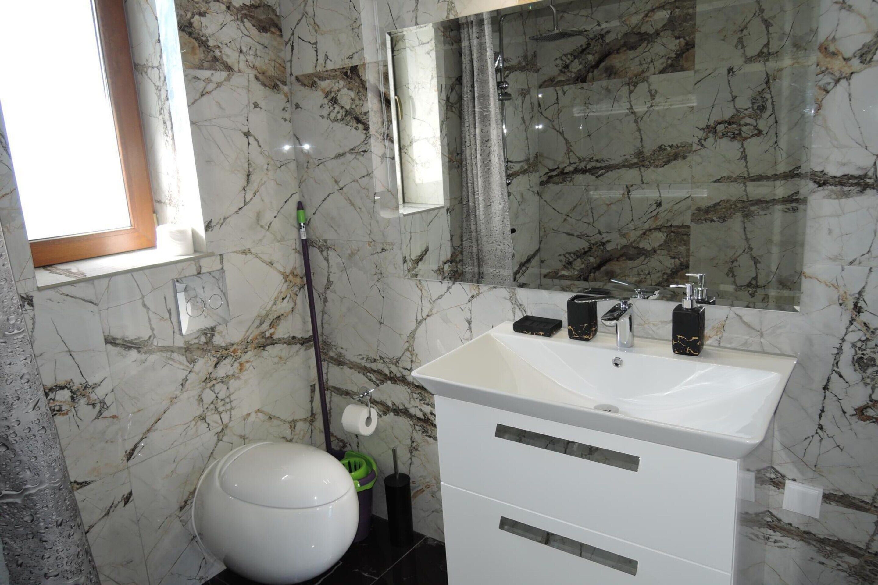 Un baño con lavamanos blanco, espejo y paredes de mármol.