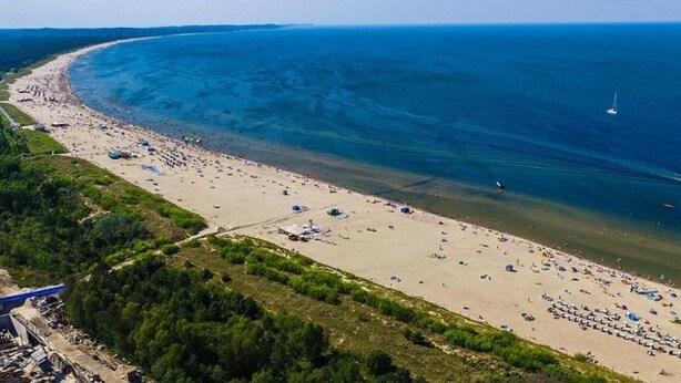 An aerial view of a beach with a curved shoreline, numerous beach umbrellas, and a jet ski in the water.