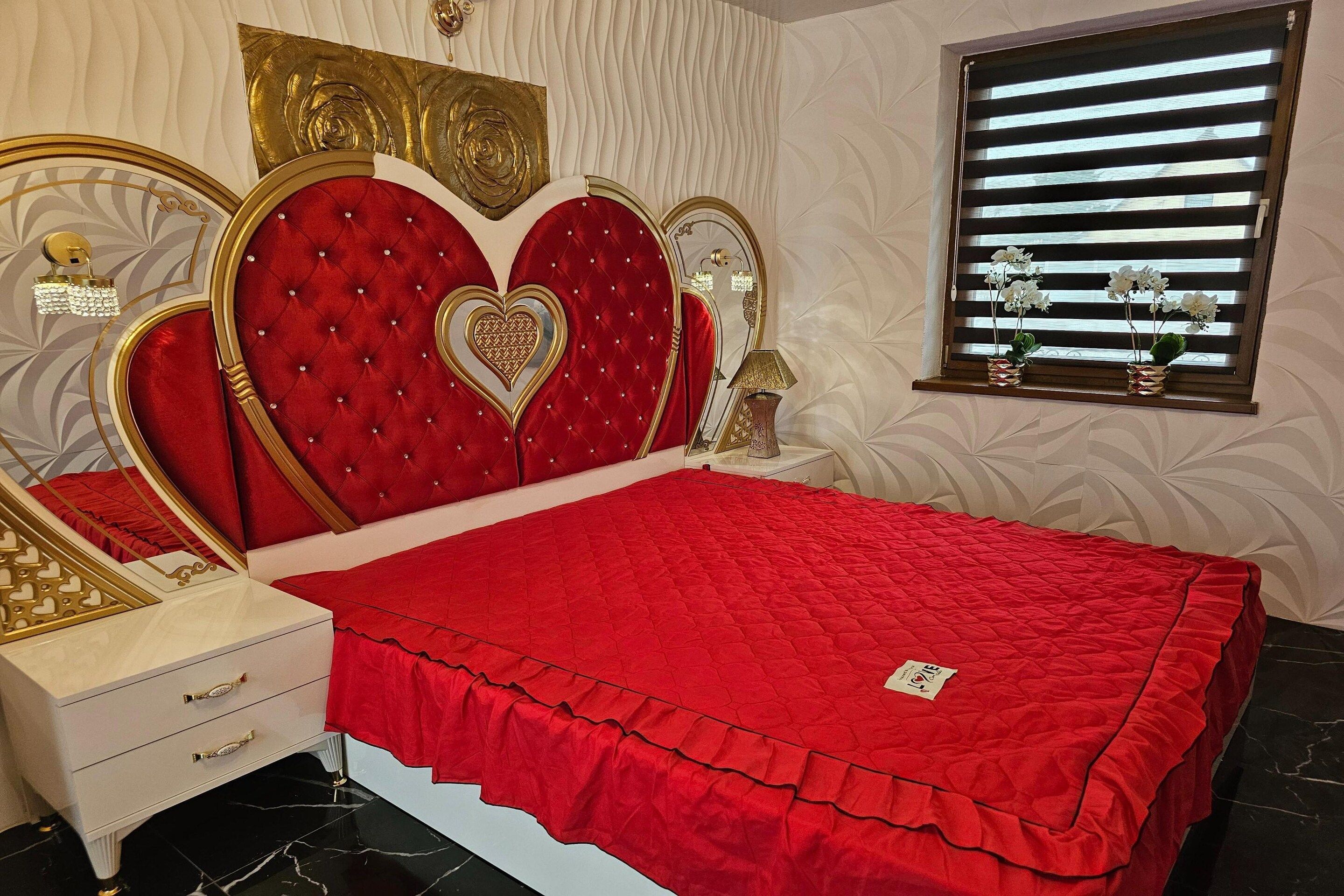 A bedroom with a red bedspread, a white bedside table, and a decorative headboard.