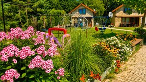 A garden with flowers, a swing set, and a house with a stone facade.