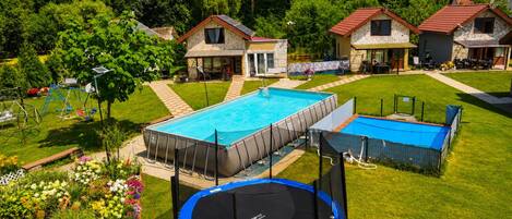 A residential area with a swimming pool, a trampoline, and houses with stone facades.