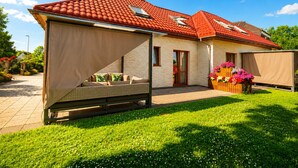 A house with a red-tiled roof, a covered patio with a sofa, and a garden with flowers.