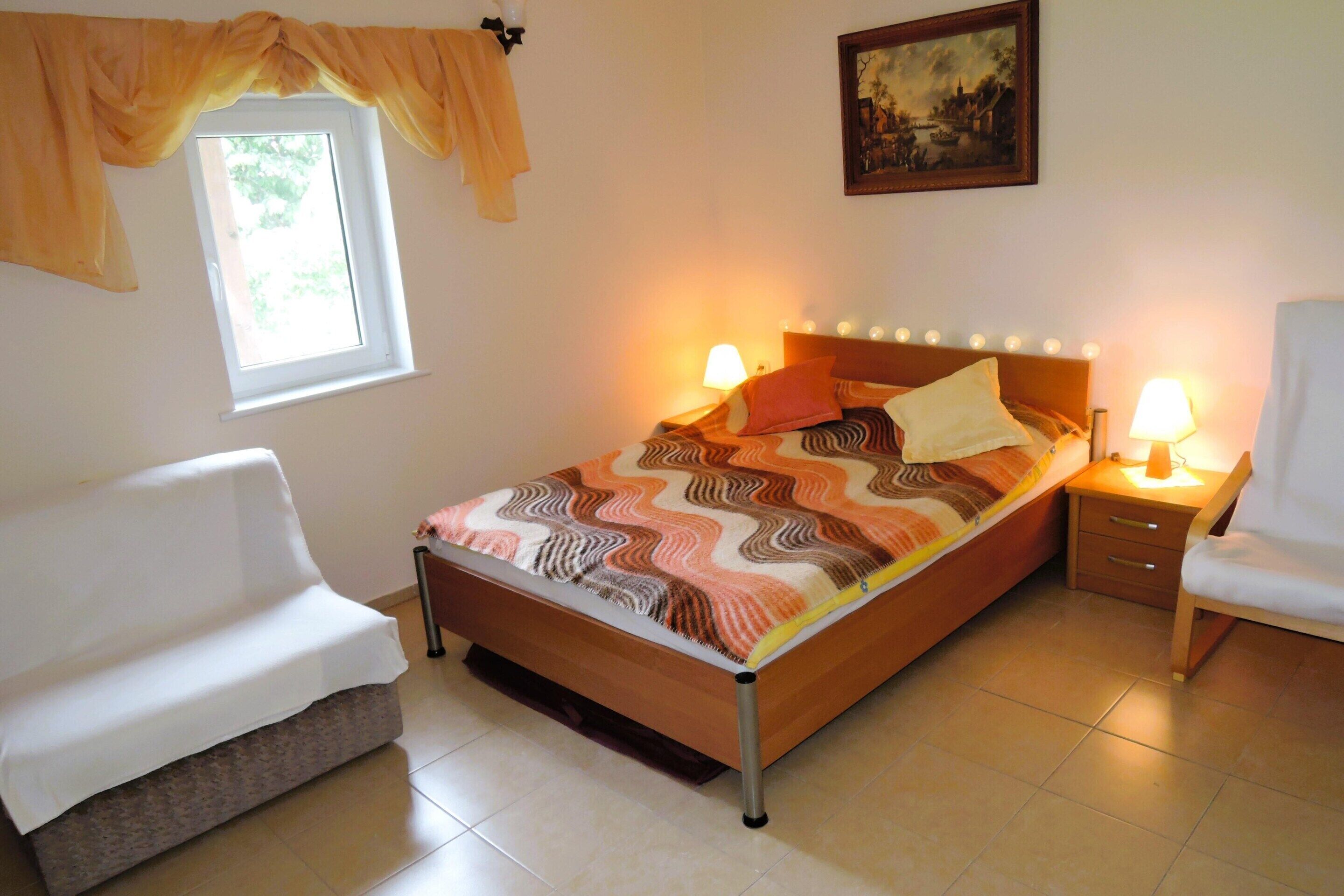 A neatly arranged bedroom with a bed, bedside tables, a chair, and a window with curtains.
