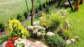 Un jardín con un columpio, una zona delimitada por una cerca y diversas plantas.