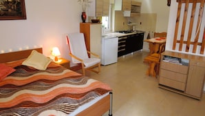 Un dormitorio con cama, una silla, un escritorio y una kitchenette.