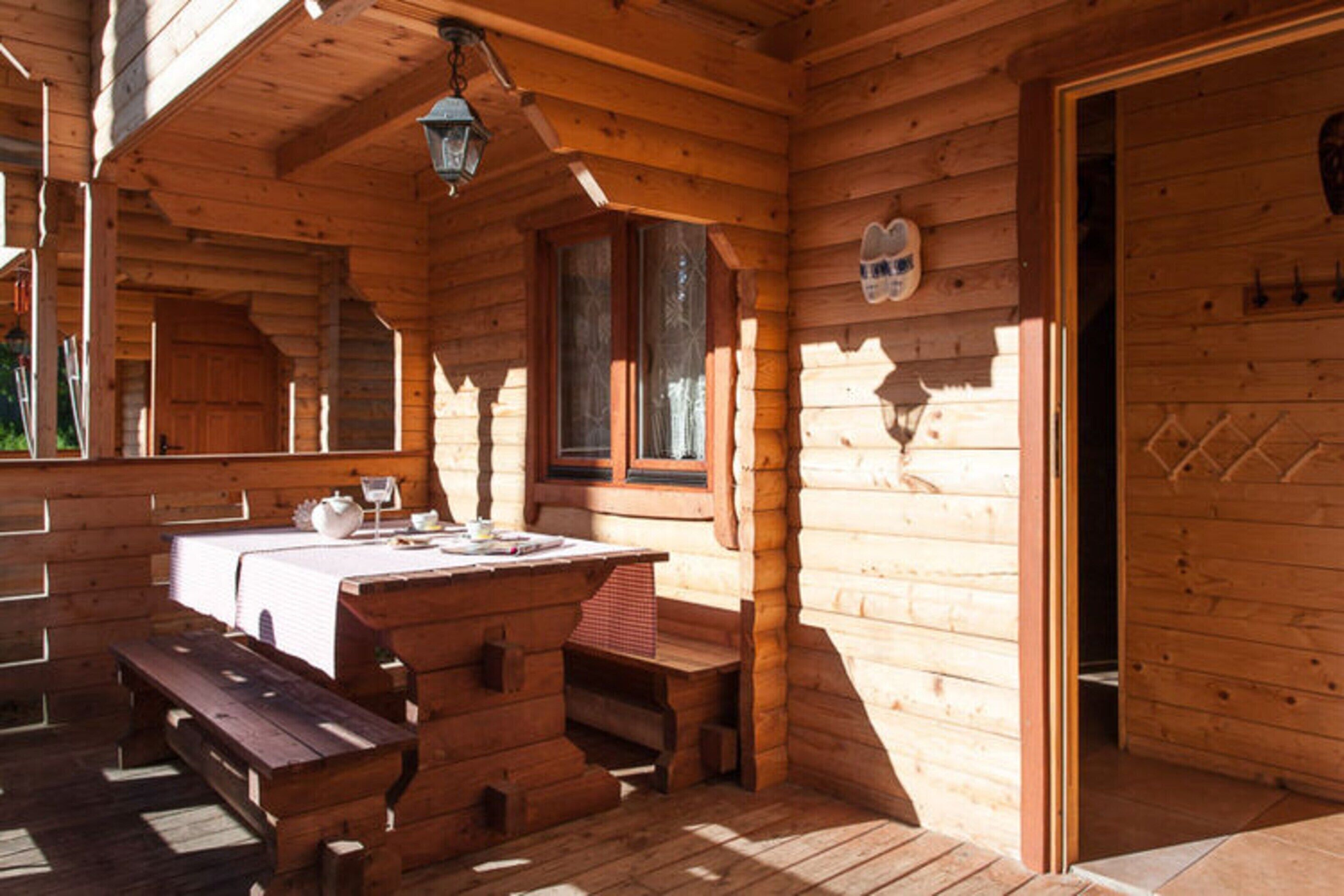 A wooden cabin with a wooden bench, a table with a white tablecloth, and a window with a view.