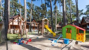 A playground with sand and play equipment, surrounded by wooden cabins. - Holiday Cottage in Pobierowo Near Baltic Beach (Rewal)