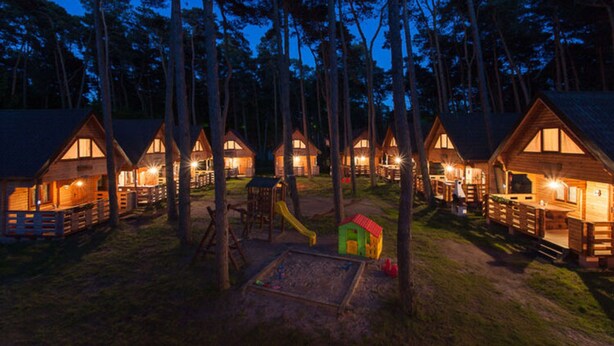 A row of wooden cabins with a playground in the center, surrounded by trees. - Holiday Cottage in Pobierowo Near Baltic Beach (Rewal)