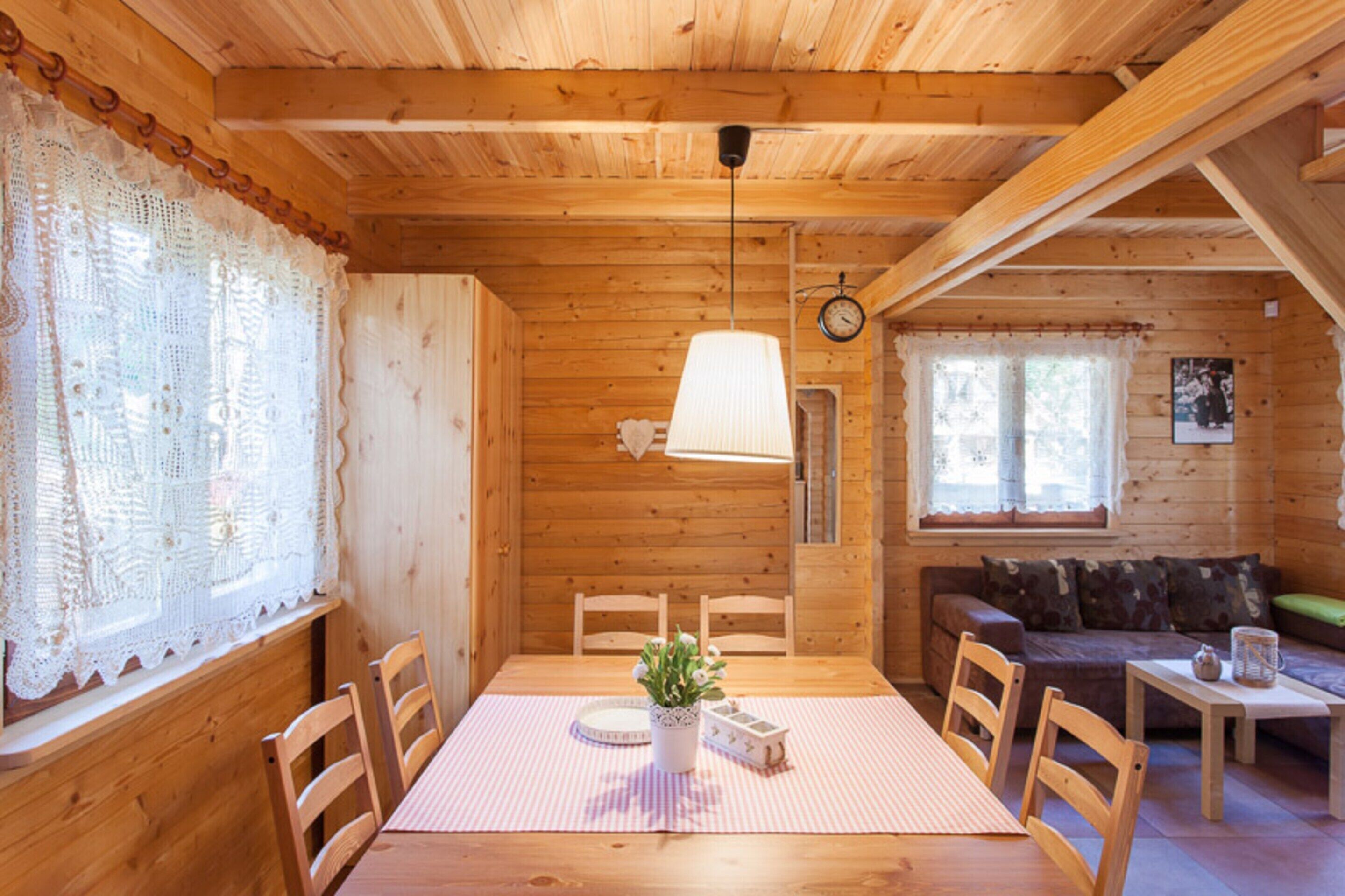 A cozy wooden cabin interior with a dining table, chairs, a sofa, and a small table with a teapot.