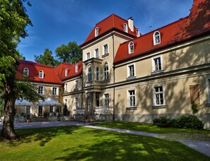 Stately building with a grand entrance and covered porch, set amidst a serene lawn and trees.