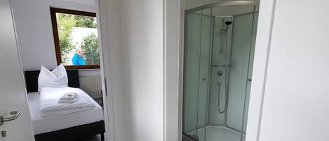 A modern hotel room with a bed, a glass-enclosed shower, and a view of the outdoors.