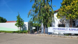 A building with a white facade, a sign reading "ZIMMERWELT ILSFELD," and a gated entrance.