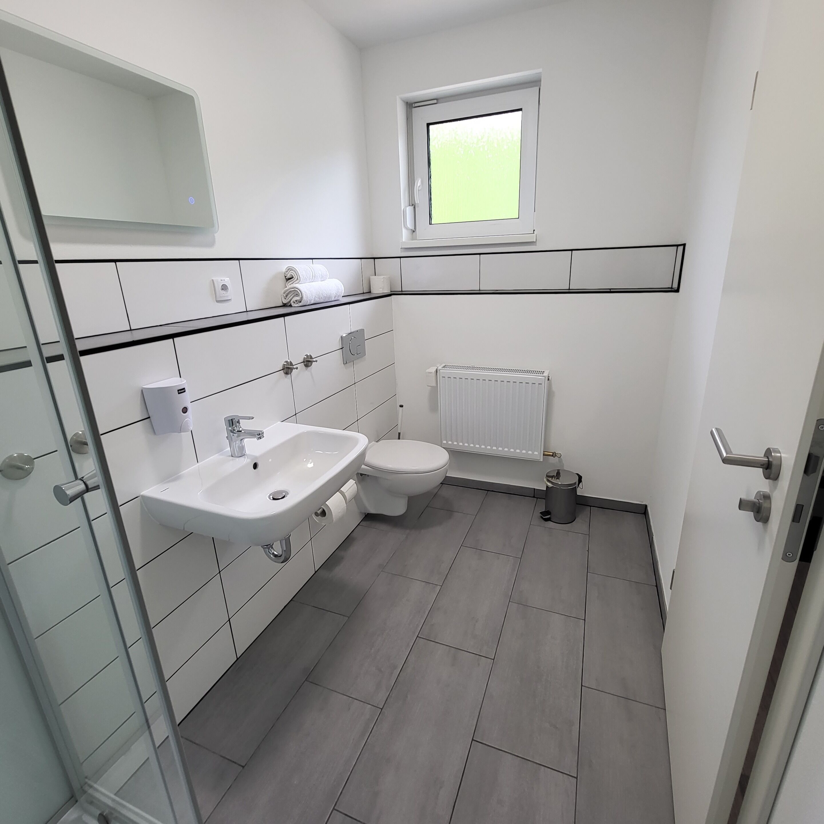 Un baño moderno con un lavamanos blanco, inodoro y una ventana sobre el inodoro.