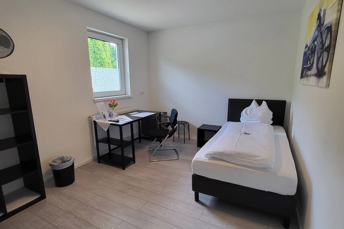 A modern bedroom with a bed, desk, chair, and a small window.