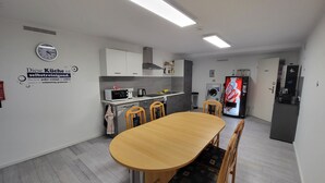 A modern kitchen with white cabinets, a microwave, and a coffee maker. There is a dining table with chairs and a wall clock.