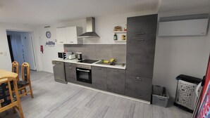 A modern kitchen with grey cabinets, a stainless steel range hood, a built-in oven, and a sink. There is a dining area with a wooden table and chairs.