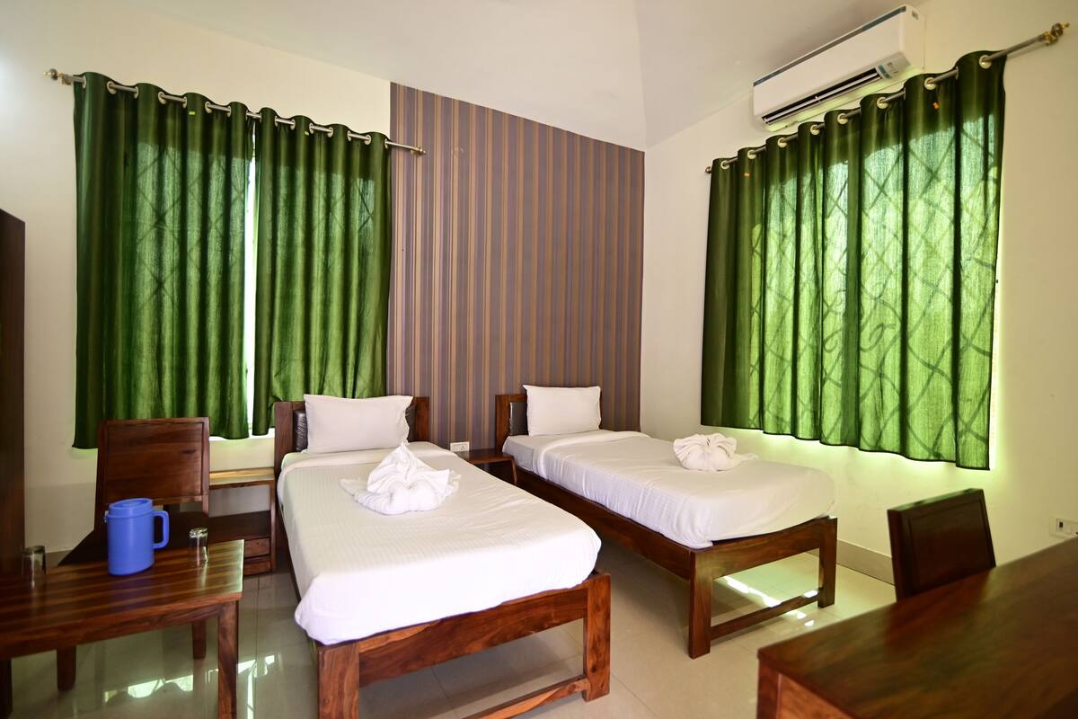 A hotel room with two single beds, a wooden desk, a chair, and a table.