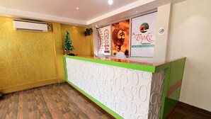 Un espace d’accueil doté d’un plancher en bois, d’un comptoir de réception aux couleurs vertes et blanches, et d’un climatiseur fixé au mur.