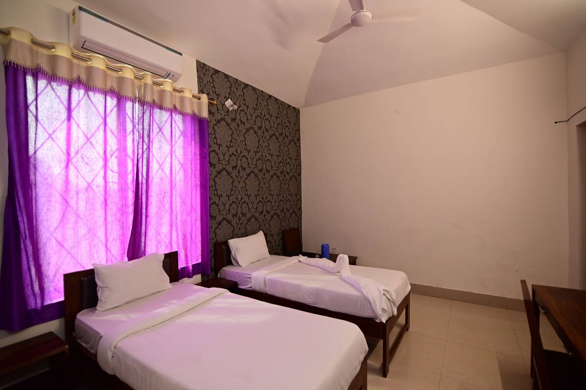 A hotel room with two single beds, a ceiling fan, an air conditioning unit, and a patterned wallpaper on the wall.