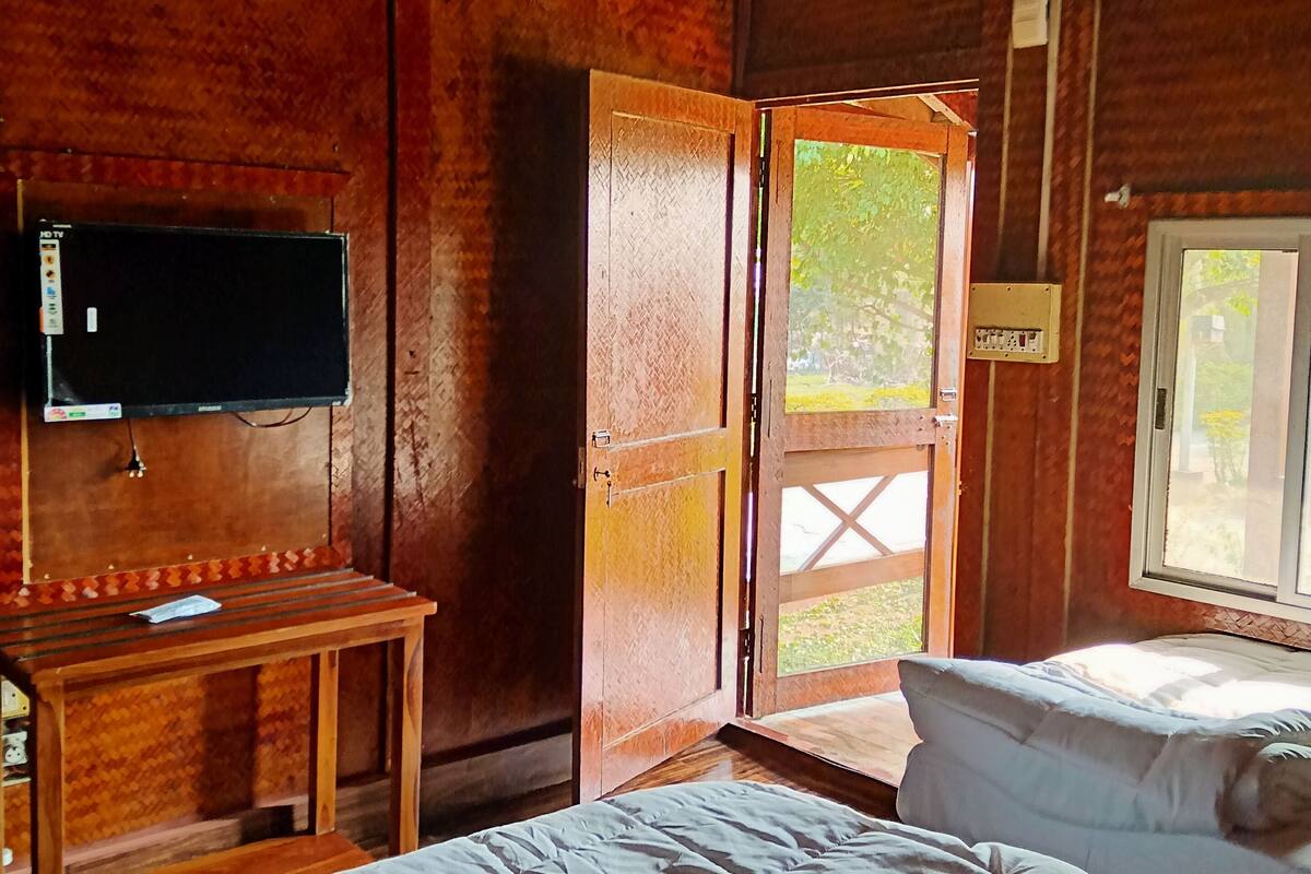 A wooden room with a bed, a desk, a TV, and a door leading outside.