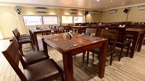 Une salle de conférence dotée de tables et de chaises en bois, de climatiseurs et d’un écran de projection.
