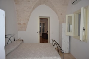 A bedroom with a bed, a wardrobe, and an arched doorway leading to another room. - Villa in Puglia Near Ostuni Marina (Ostuni)