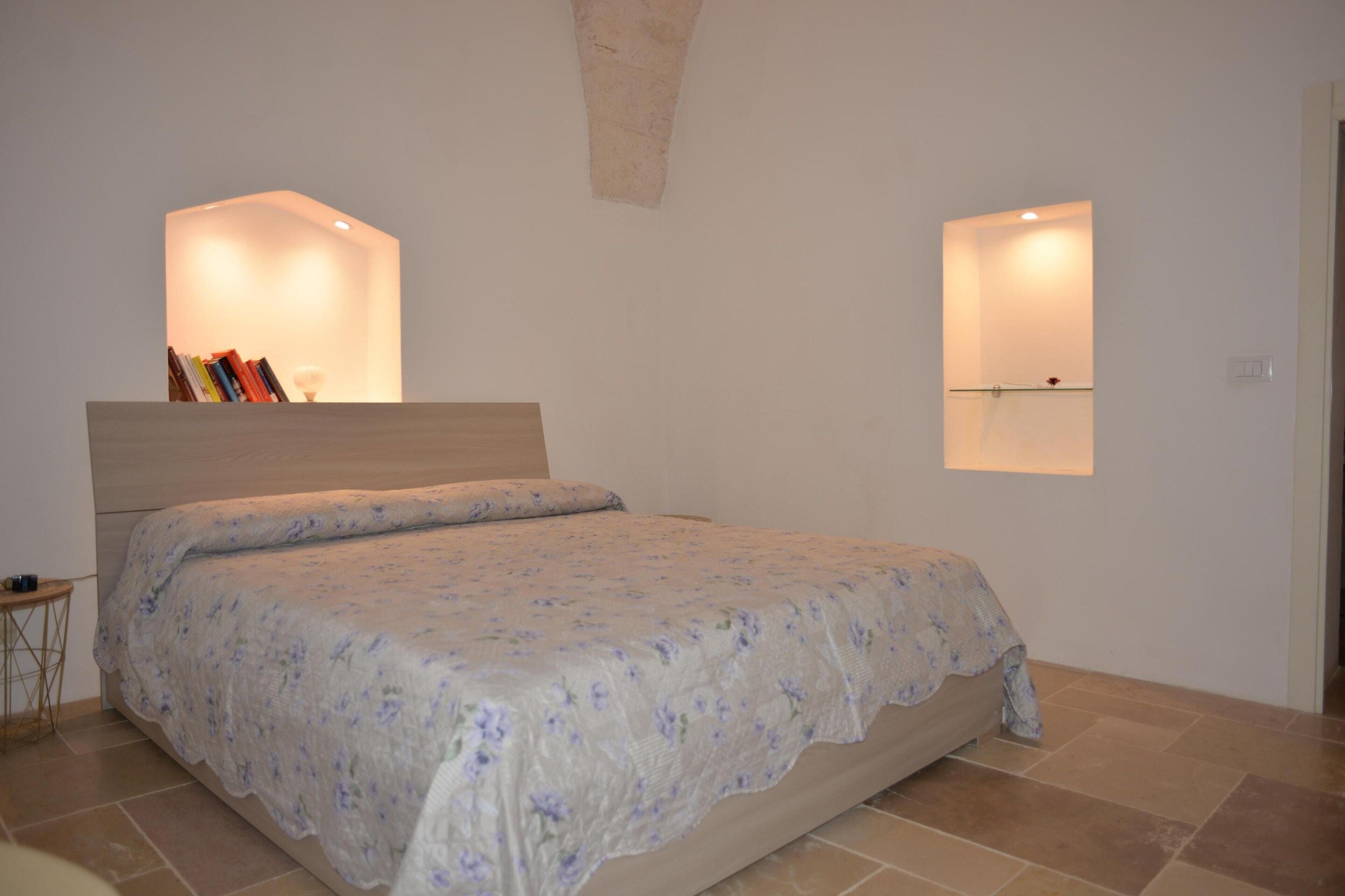 A bedroom with a bed, a nightstand, and two wall-mounted reading lights.