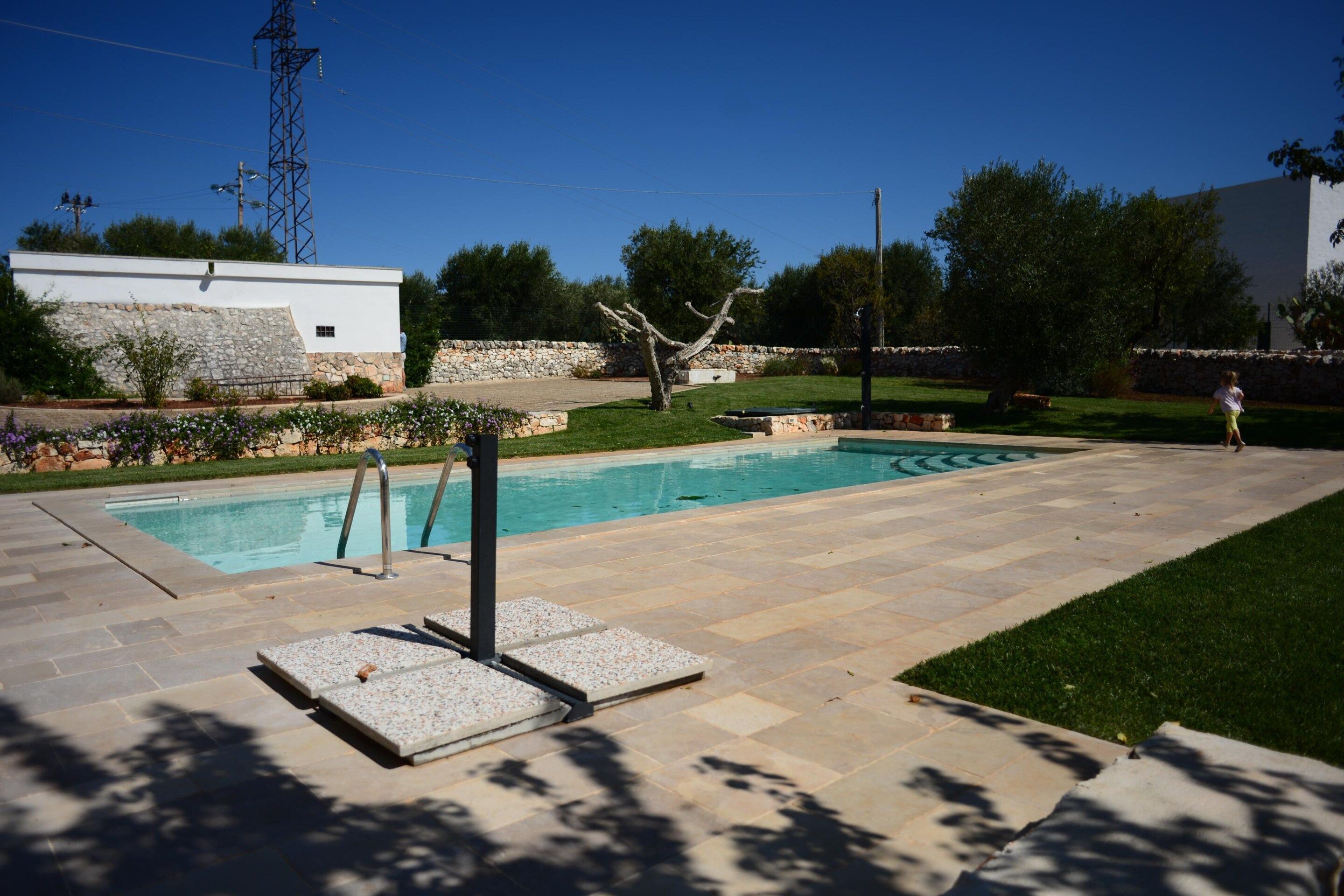 Una piscina con bordo in pietra, circondata da un'area verde e un muro in pietra.