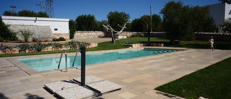 Una piscina con solárium de piedra, rodeada de césped y un muro de piedra.