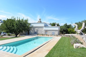 A swimming pool with a stone wall and a modern building in the background. - Villa in Puglia Near Ostuni Marina (Ostuni)