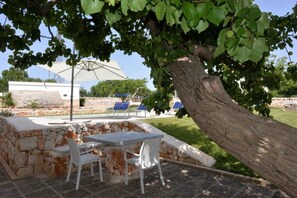 An outdoor seating area with stone walls, white chairs, and a table. - Villa in Puglia Near Ostuni Marina (Ostuni)