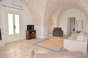 A spacious living area with a high arched ceiling, a television on a wooden cabinet, a brown armchair, a white sofa, and a patterned rug. - Villa in Puglia Near Ostuni Marina (Ostuni)