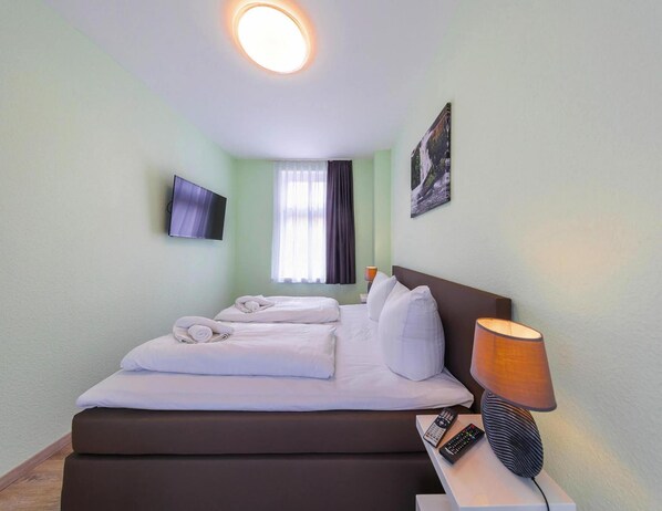 A hotel room with a bed, a TV, a lamp, and a painting on the wall.