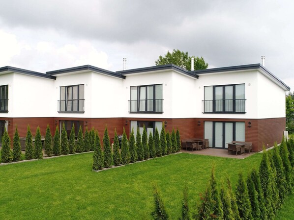 A modern two-story residential building with a flat roof, large windows, and a well-maintained lawn with neatly trimmed hedges. - Ferienhaus in Damp Nahe Ostseestrand (Damp)