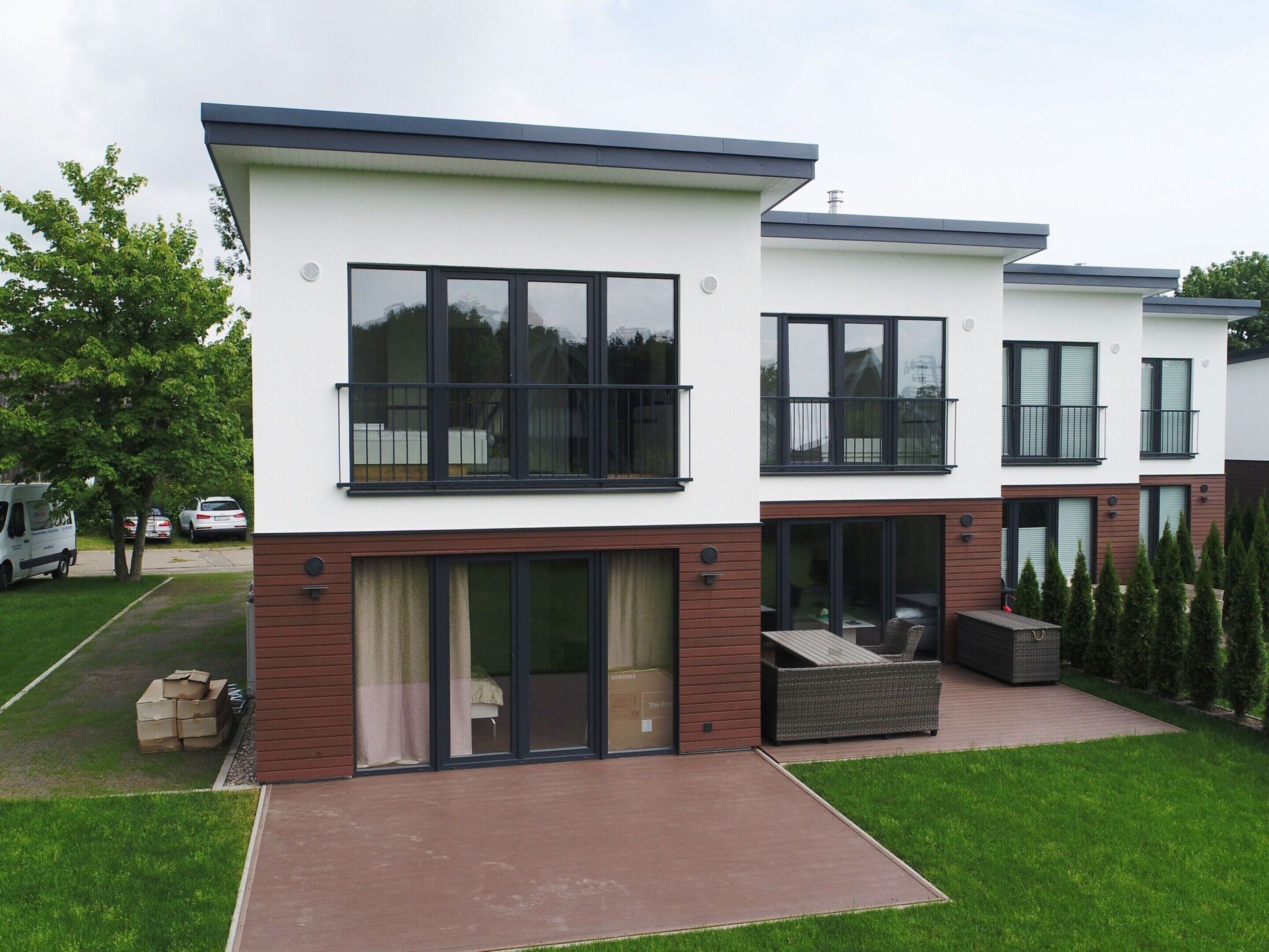 A modern two-story residential building with large windows, balconies, and a covered patio area.