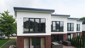 A modern two-story residential building with large windows, balconies, and a covered patio area. - Ferienhaus in Damp Nahe Ostseestrand (Damp)