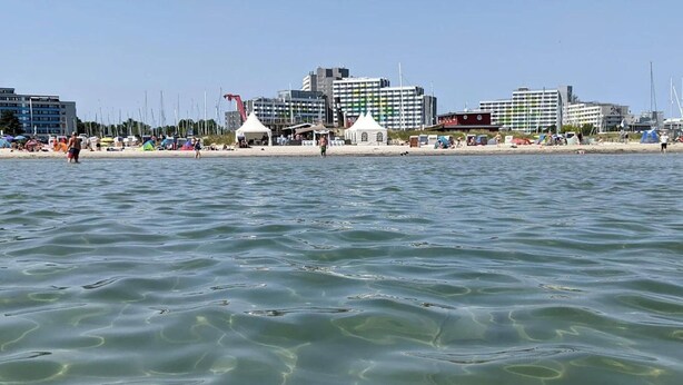 A beach with clear water, tents, and buildings in the background. - Ferienhaus in Damp Nahe Ostseestrand (Damp)