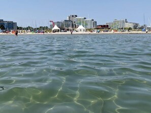 Una playa con agua cristalina, tiendas de campaña y edificios al fondo.