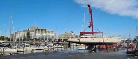 A marina with multiple boats docked, a crane, and buildings in the background.