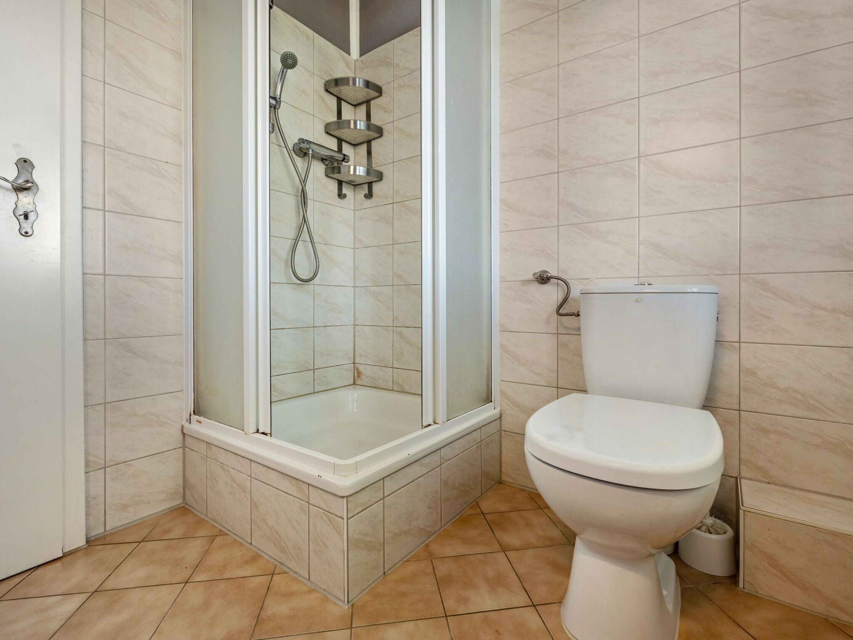 A bathroom with a glass-enclosed shower, a toilet, and a corner sink.