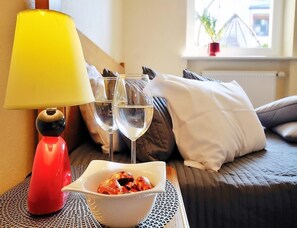 Een bed met kussens, een nachtkastje met een lamp, twee wijn glazen en een schaal eten.