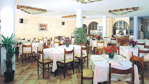 A restaurant with multiple tables and chairs, a large potted plant, and a tiled floor.