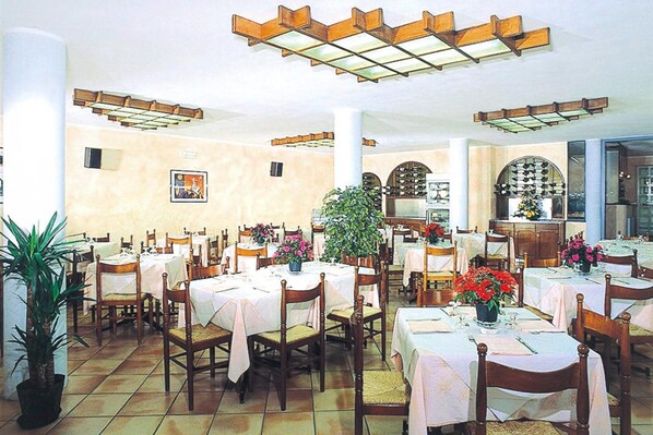 A restaurant with multiple tables and chairs, a large potted plant, and a tiled floor. - Apartment in Pietra Ligure (Pietra Ligure)