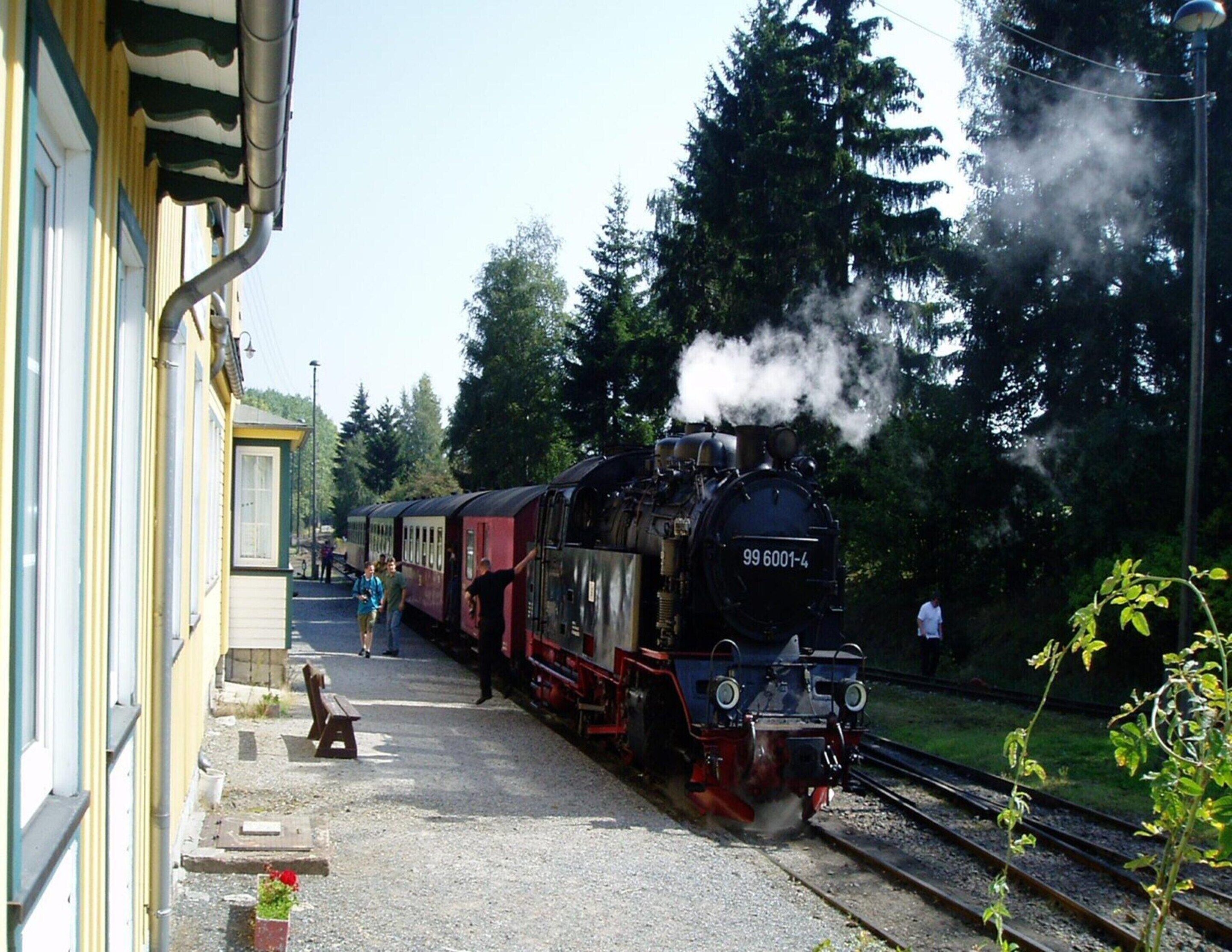 Una locomotora de vapor, número 99 6001-4, en una estación con pasajeros subiendo.