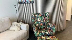Une pièce avec un mur à rayures, un canapé, un fauteuil à motifs floraux et un tableau représentant des voiliers.