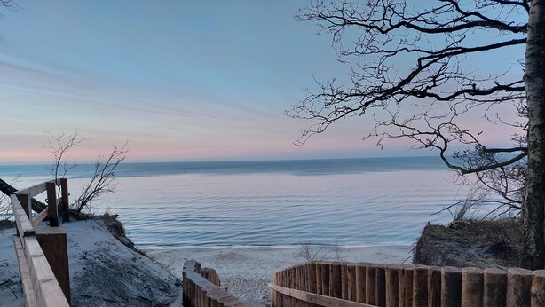 A wooden staircase leading down to a sandy beach with a wooden fence and a tree in the background. - Wooden House in Kolczewo Near Baltic Sea Beach (gmina Wolin)
