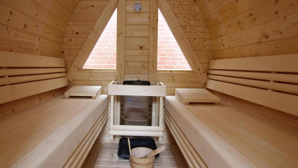 A sauna room with wooden benches, a bench heater, and a bucket. - Ferienwohnung in Westerland (Sylt)