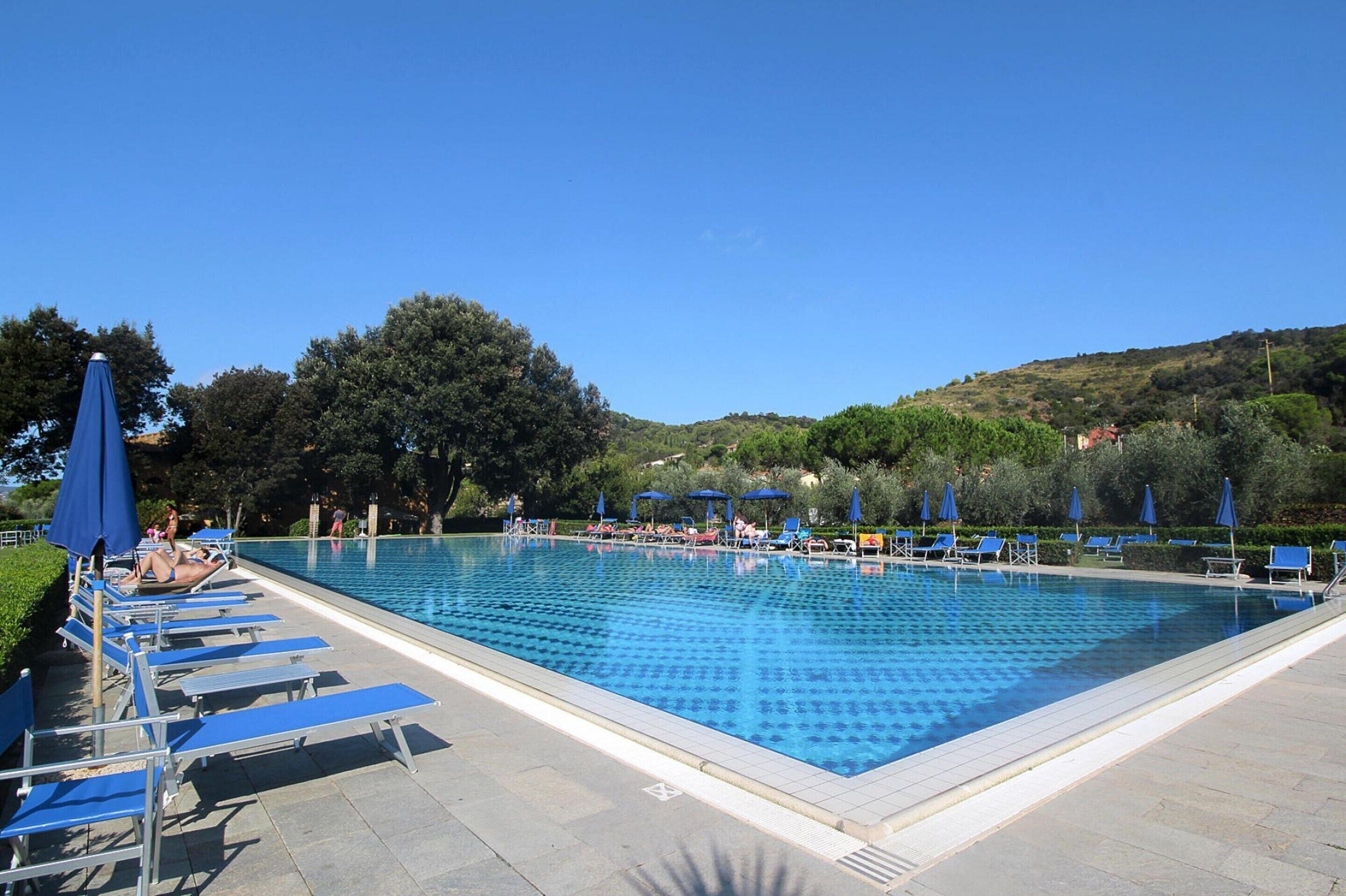 Ein rechteckiger Swimmingpool mit blauem Wasser, umgeben von Liegestühlen und Sonnenschirmen.